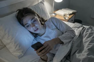 Adolescente fatiguée utilisant son smartphone tard le soir dans sa chambre, illustrant les effets des écrans sur le sommeil des jeunes